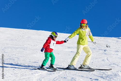 Mother teaching kid son skiing in snowy mountains