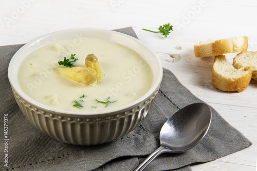white asparagus cream soup with with parsley garnish in a bowl and bread, gray napkin on a white table, copy space