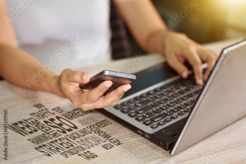 A woman's hand working on a laptop computer and interactive technology online on a smartphone.