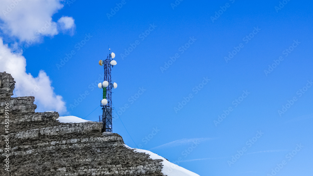 Communication tower in high alpine mountains against clear blue sky background