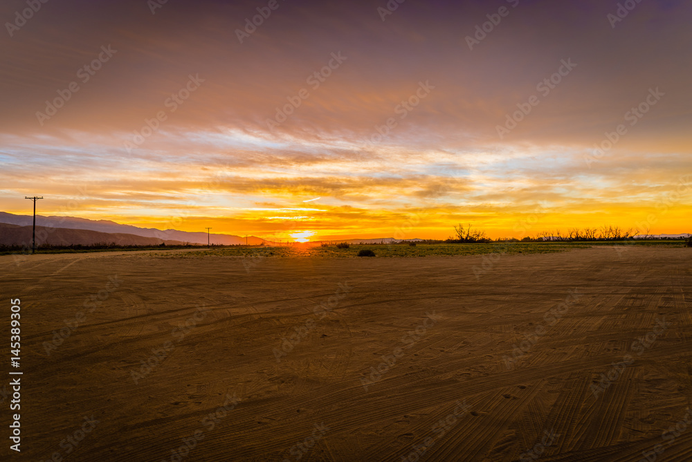 Desert sunrise over an empty dirt parking lot with mountains and telephone poles in the background. Desert sunrise over an empty dirt parking lot with mountains and telephone poles in the background.