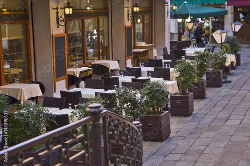 Fototapeta Naklejka Na Ścianę i Meble -  An empty street restaurant in the cozy courtyard of a small European city. The restaurant is waiting for visitors.