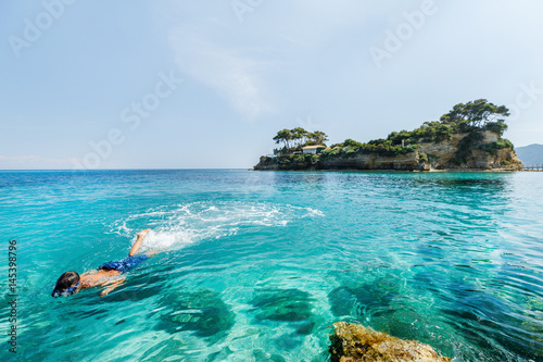 Boy snorkeling underwater in Ionian sea water at Zakinthos island in Greece. Zakinthos island popular summer Greek resort and travel destination with shallow turquoise water. Over water camera view.