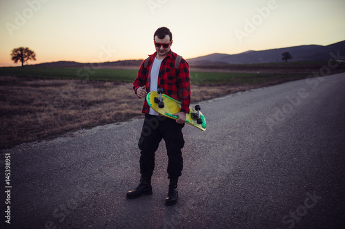 Skater man in plaid shirt holding his skateboard on the street