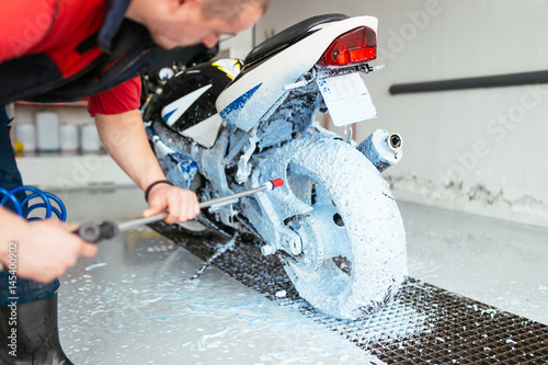A man cleaning motorcycle with sponge using blue foam, motorcycle detailing (or valeting) concept. Selective focus. 