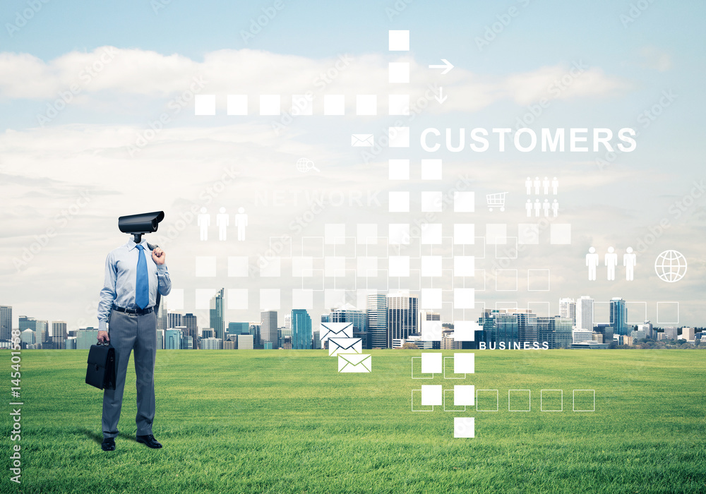 Camera headed man standing on green grass against modern citysca
