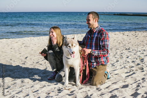 Young caucasian couple on beach with siberian husky dog