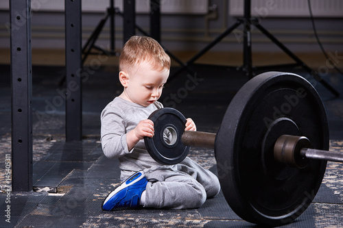 Little cute child in sportwear in the cross fit gym with a barbell. photo