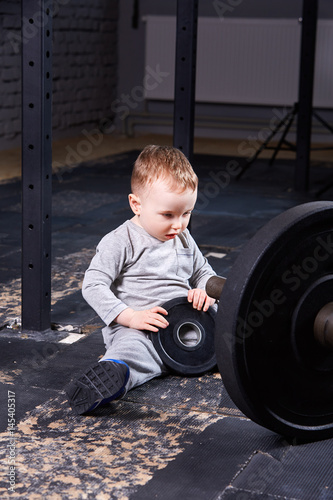 Little cute child in sportwear in the cross fit gym with a barbell. photo