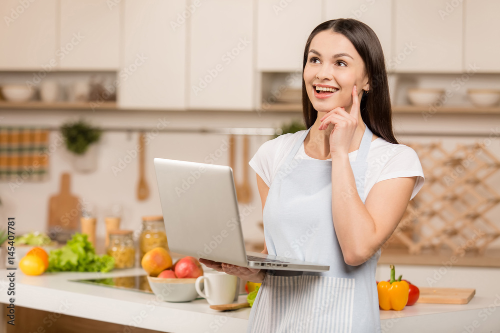 Young Woman in red shirt standing in kitchen with tablet computer, having idea and looking recipes in the kitchen. Food blogger concept