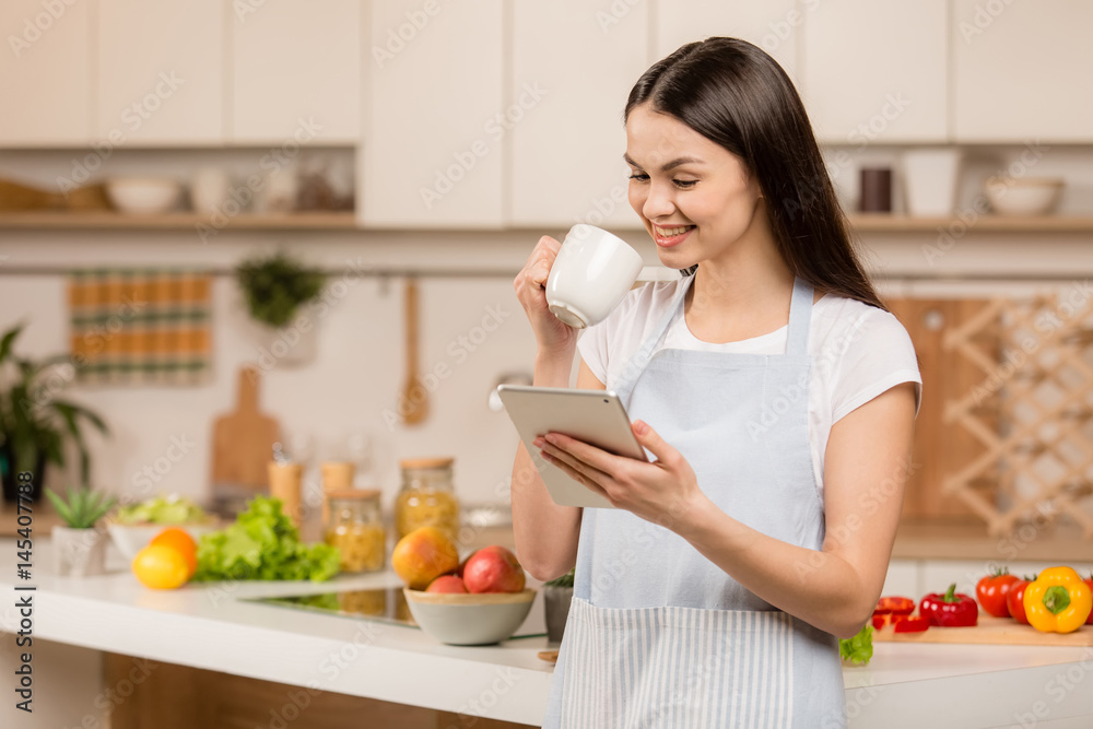 Young Woman standing in kitchen with tablet computer and looking recipes. Food blogger concept