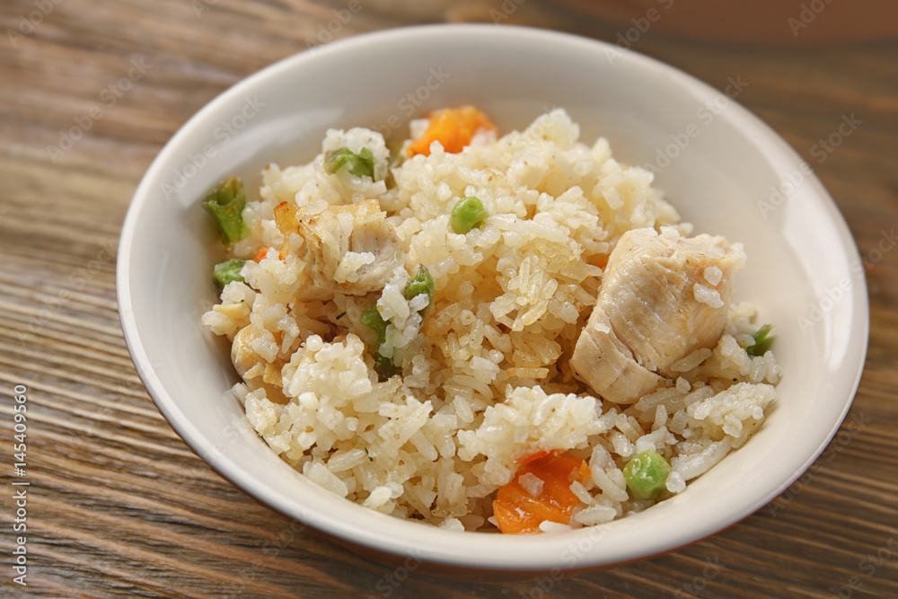 Delicious rice with chicken and vegetables in plate on wooden table Delicious rice with chicken and vegetables in plate on wooden table