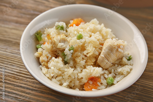 Delicious rice with chicken and vegetables in plate on wooden table