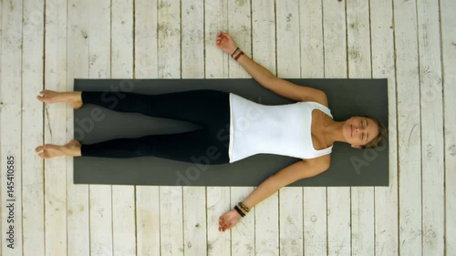 Attractive young woman working out at home, doing yoga exercise, lying in Shavasana Corpse or Dead Body Pose , resting after practice, meditating, breathing