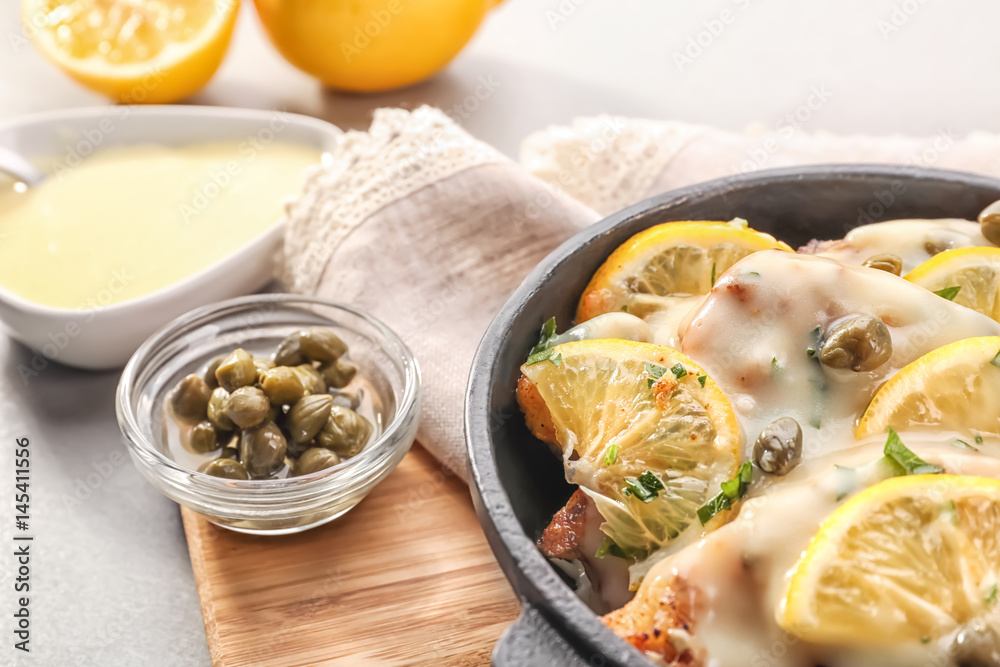 Frying pan with delicious chicken piccata on wooden board Frying pan with delicious chicken piccata on wooden board