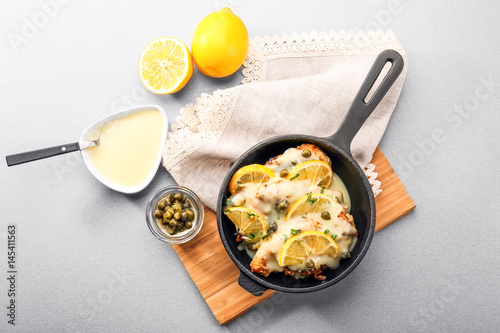 Frying pan with delicious chicken piccata on wooden board