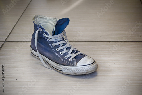 Old but whole blue sneaker with traces of road dust and dirt on the floor, hdr