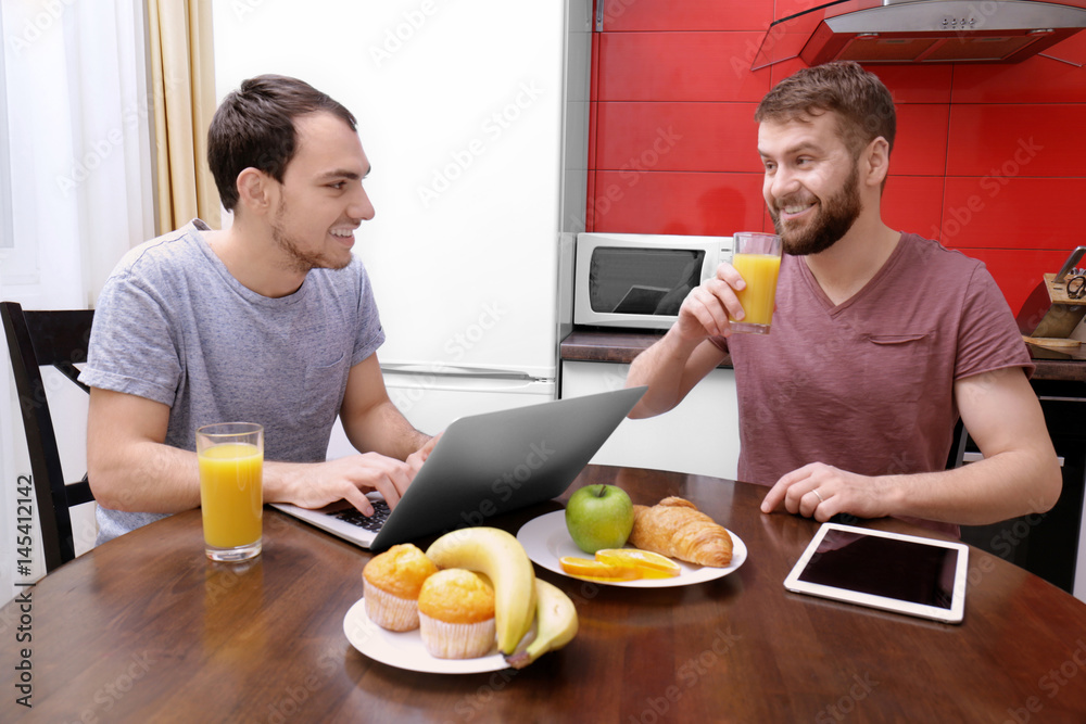Happy gay couple having breakfast in kitchen at home Happy gay couple having breakfast in kitchen at home