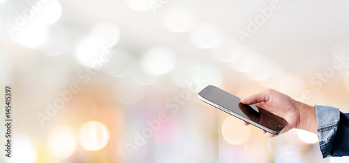 Hand using smart phone over blur store with bokeh light background, banner, business and technology concept, digital marketing, seo, e-commerce, lifestyles, social media network