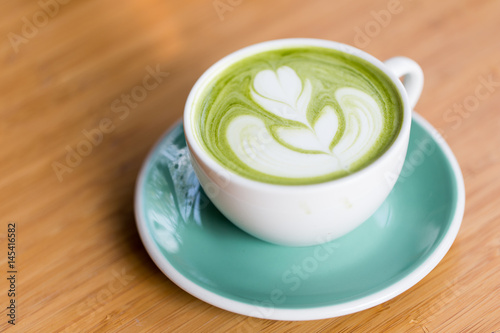 Hot matcha green tea with shape latte art in green cup on wood table. Coffee time conception.