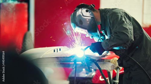 Tableau sur toile Welding industrial: worker in helmet repair detail in car auto service - blue sp