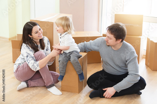 Happy young family with unpacking boxes at new home on moving day
