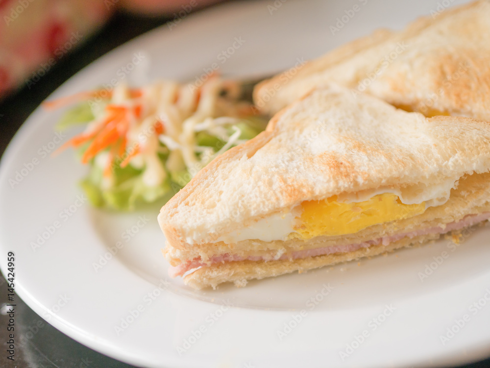 Closeup of triangle chopped sandwich including of egg, ham and bacon in white plate. Sandwich is a popular dish for breakfast.