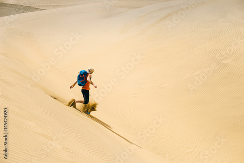 Man with a backpack runs on hot yellow sand in the desert