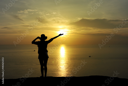 Silhouette of woman raising hands at sunset