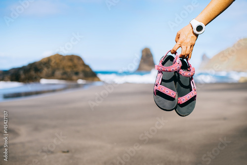 Girl holds pink sandals and walks on warm sand by the ocean photo