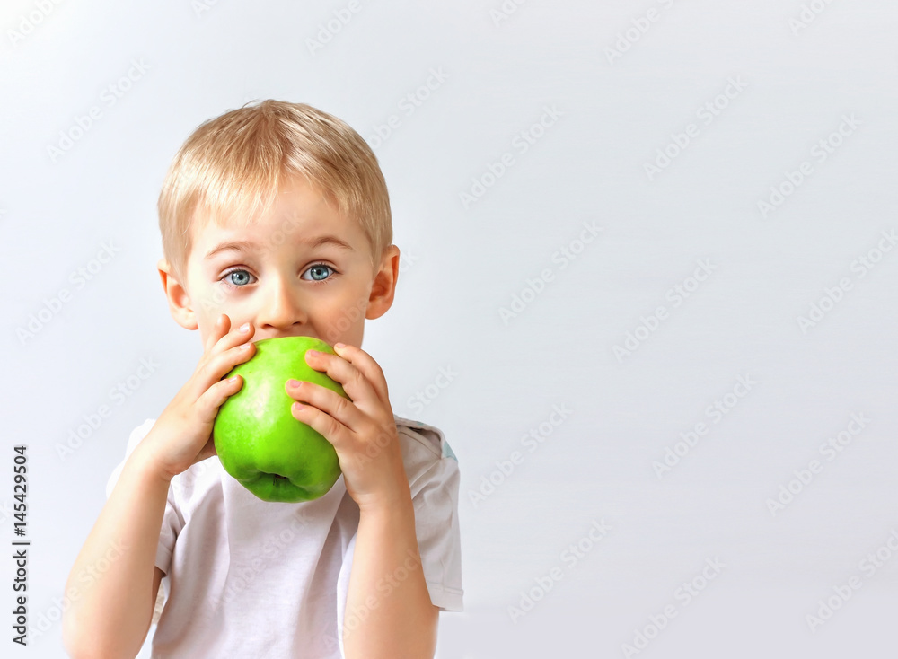 Happy cheerful boy eats the big apple, the child is the fruit green, soft focus Happy cheerful boy eats the big apple, the child is the fruit green, soft focus