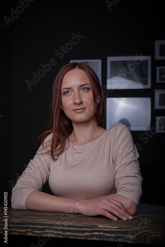 Beautiful young woman sitting at vintage wooden table. Wore long classic dress and shoes. Low key studio shot, large portrait with hands.