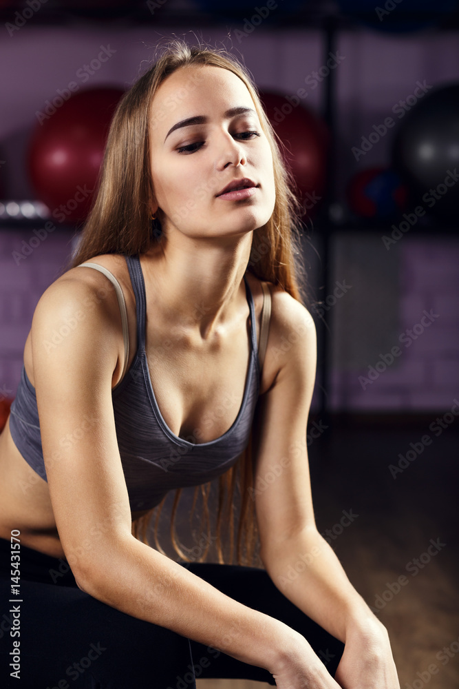 Portrait of younf fitness girl with perfect skin and body sitting in gym Portrait of younf fitness girl with perfect skin and body sitting in gym