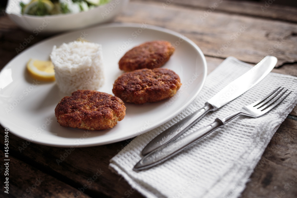 Three croquettes on white ceramic plate with cutlery aside on wooden table Three croquettes on white ceramic plate with cutlery aside on wooden table
