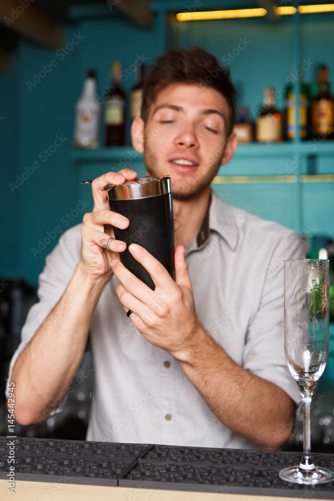 Young handsome barman in bar shaking and mixing alcohol cocktail Young handsome barman in bar shaking and mixing alcohol cocktail