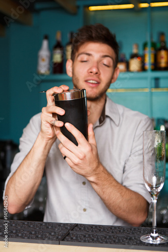 Young handsome barman in bar shaking and mixing alcohol cocktail