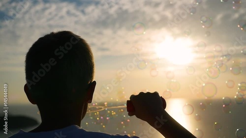 The boy is making soap bubbles. Closeup. Panoramic view. Sunset photo