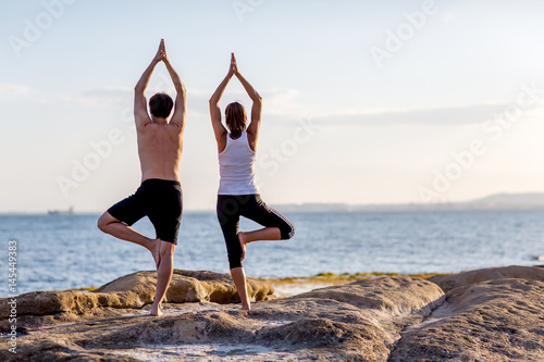 A couple is doing yoga exercises at the seashore of Mediterranean sea