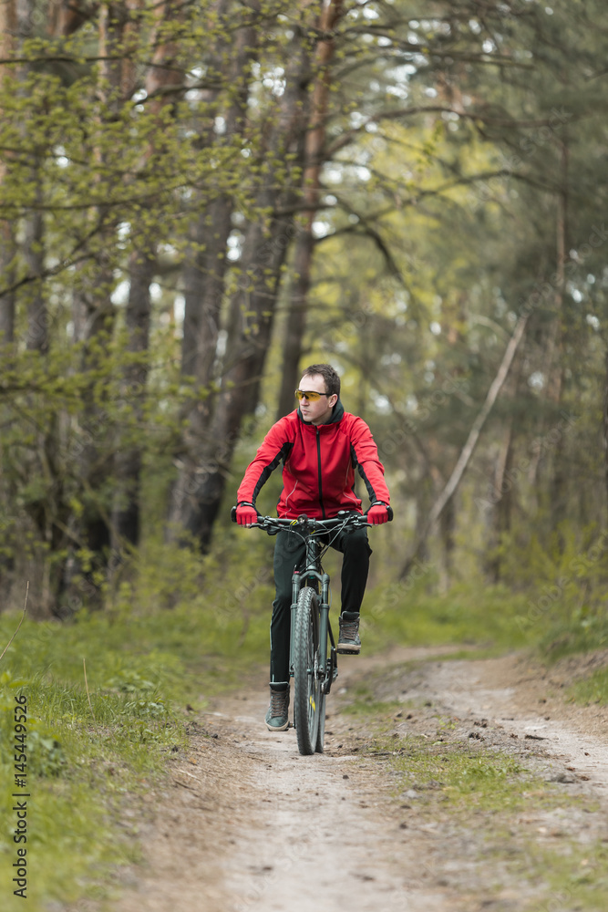 Young attractive man wears red suit ride the bike on the forest road
