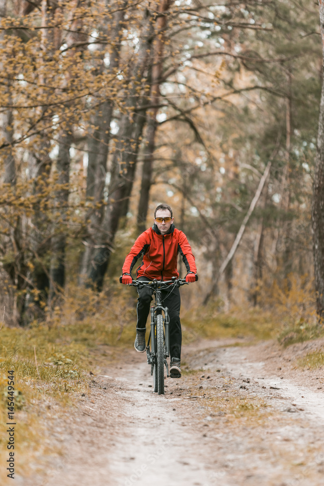 Obraz premium Young attractive man wears red suit ride the bike on the forest road