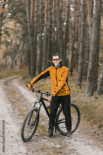 Young attractive man wears yellow suit on bike in the forest