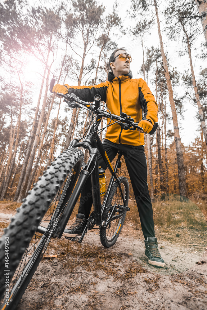 Young attractive man wears yellow suit ride the bike on the forest road Young attractive man wears yellow suit ride the bike on the forest road