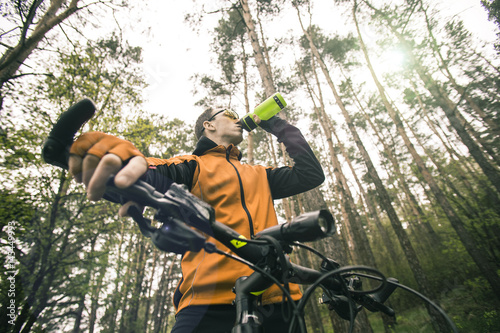 Young attractive man wears yellow suit drink water from sport bottle in the forest