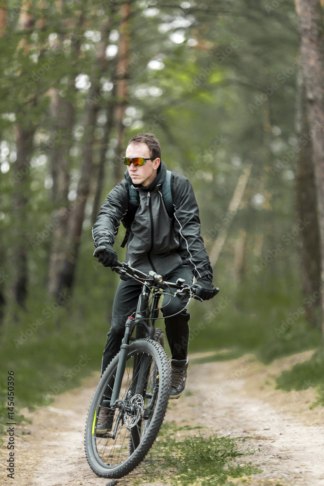 Fototapeta premium Young attractive man wears dark suit ride the bike on the forest road