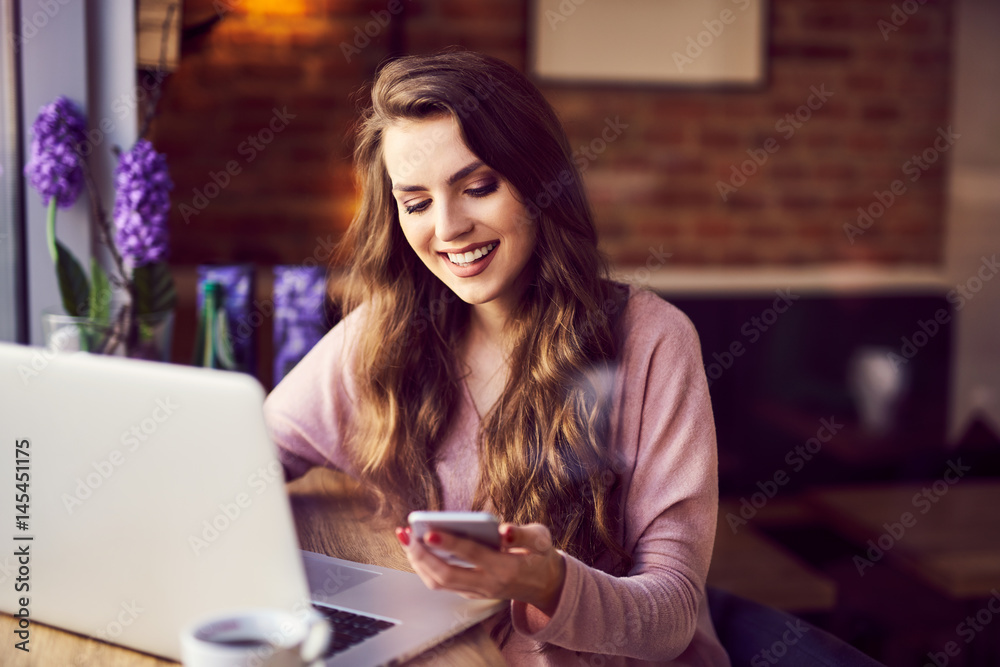 Attractive young woman with laptop chacking message on her phone at coffee shop Attractive young woman with laptop chacking message on her phone at coffee shop