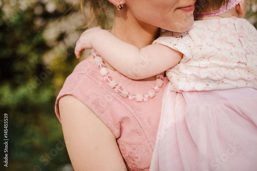 A little girl hugs Mom by the neck. The girl is in her mother's arms.