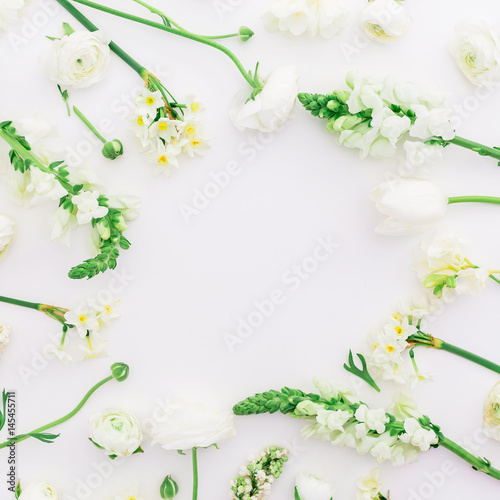 Round frame of white ranunculus, snapdragon, lilac and tulip on white background. Flat lay, top view.