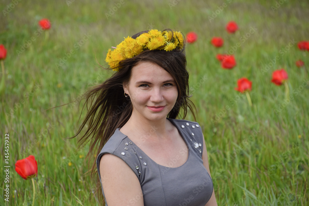 A girl with a wreath of dandelions on her head. Beautiful fairy young girl in a field among the flowers of tulips. A girl with a wreath of dandelions on her head. Beautiful fairy young girl in a field among the flowers of tulips.