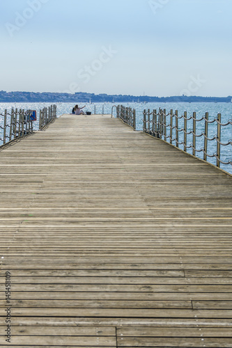 Two girls / young women sitting on pier and making selfies with mobile phone