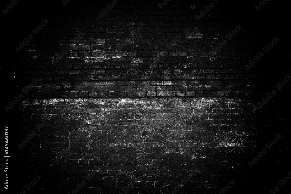 An old gloomy brick wall. Dark lighting, a light spot in the center of the brickwork. Black white empty space. Grunge background